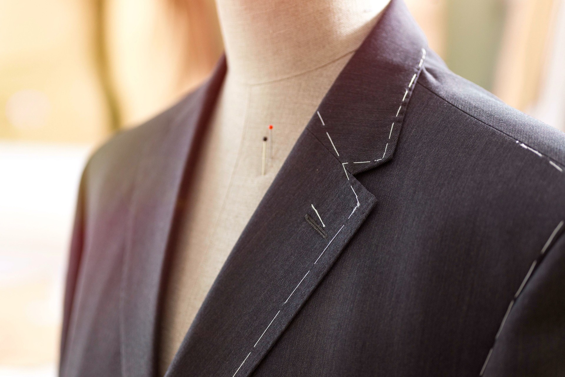Tailored suit jacket with alterations marked with basting stitch on a mannequin at bespoke tailor's workshop.